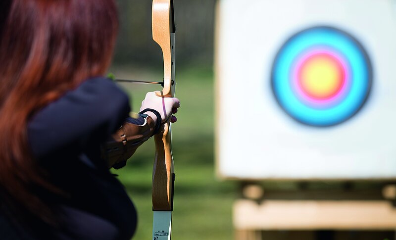 Eine Frau zielt mit einem großen Bogen auf eine Zielscheibe.